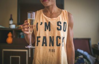 Woman holds glass of champagne while wearing a shirt that reads I'm So Fancy