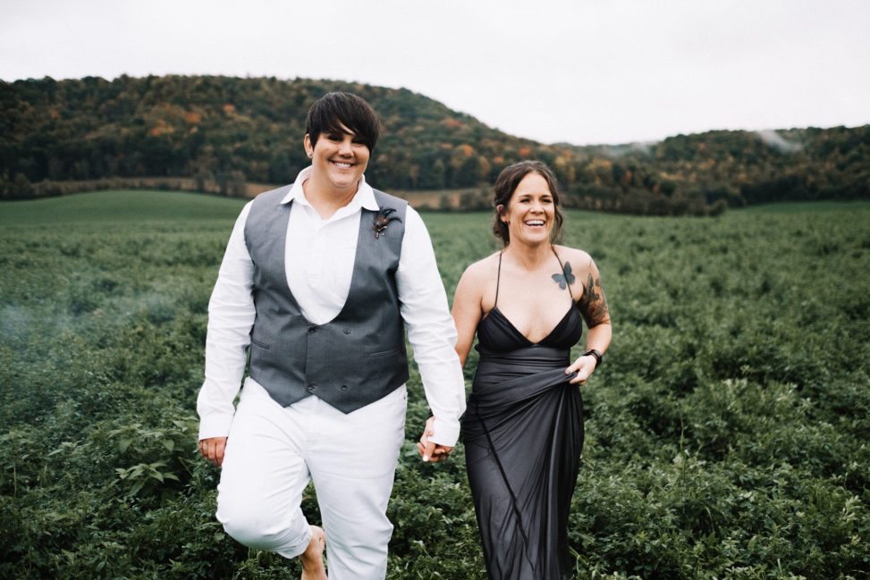 a wedding couple hold hands and walk through a field
