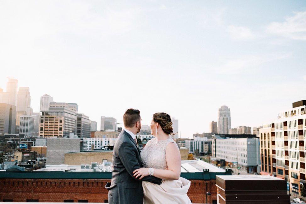 a wedding couple hold each other and look at the city