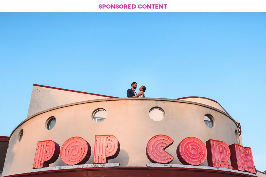 Couple stands above enormous POP CORN sign on top of a building. Sponsored Content.