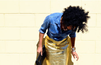Black woman standing against a wall in a gold shirt