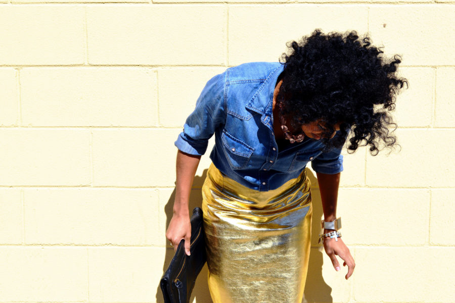 Black woman standing against a wall in a gold shirt