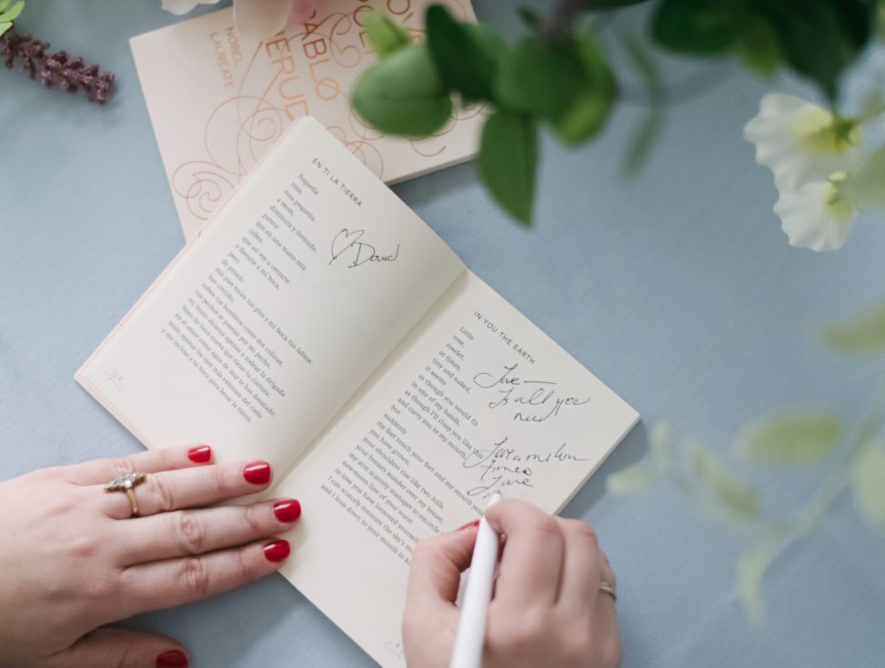woman's hands signing a poem book on a blue tablecloth