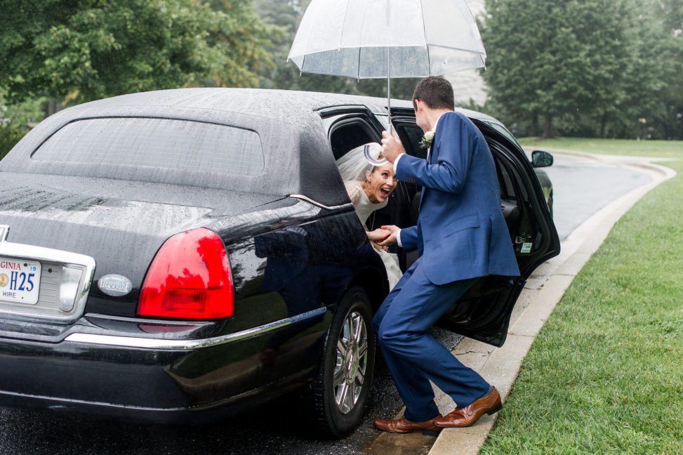 A man helps a woman step out of a limo while holding an umbrella for her