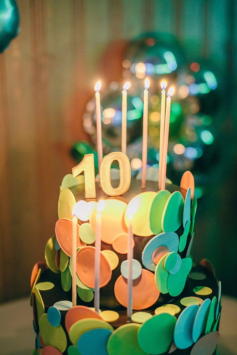 close up of a colorful tiered cake with gold candles, topped with a number 10
