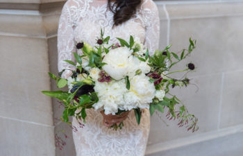 woman in white lace wedding dress holding large white and green bouquet