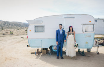 bride and groom hold hands in front of a vintage trailer in the desert