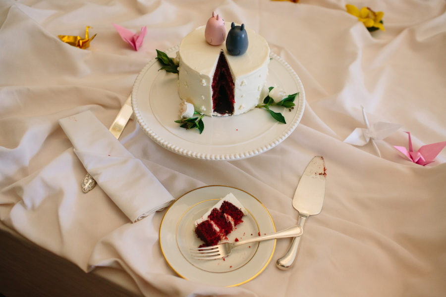 Slice of cut red velvet wedding cake on a table with flowers and white tablecloth