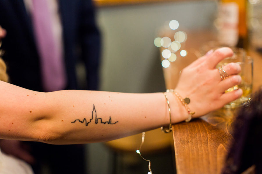Woman leaning on a bar wearing trendy delicate bracelets with a city skyline tattoo
