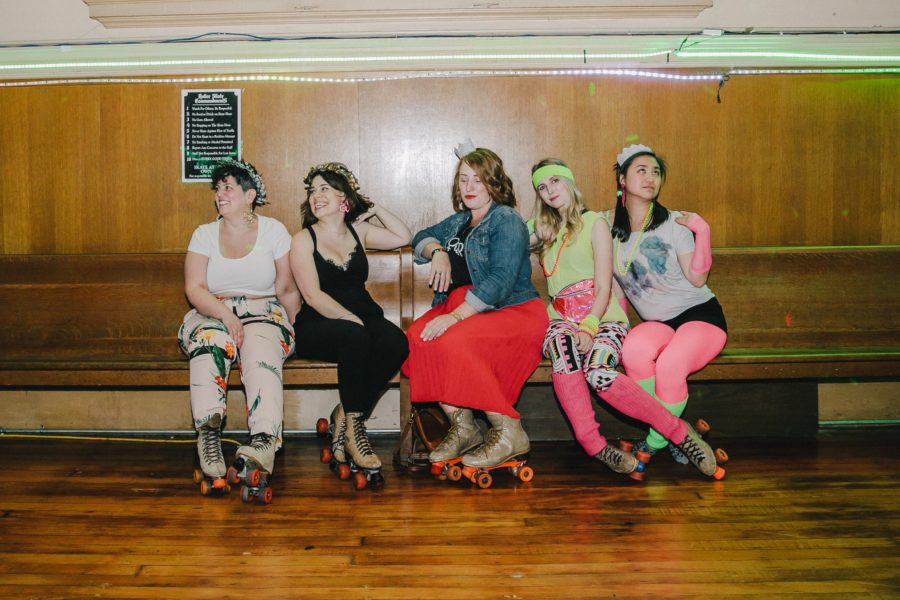 5 women in retro clothes wearing roller skates and sitting on a bench