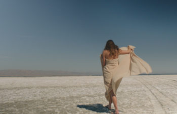 Woman walking on sand, wearing a billowing sand-colored dress