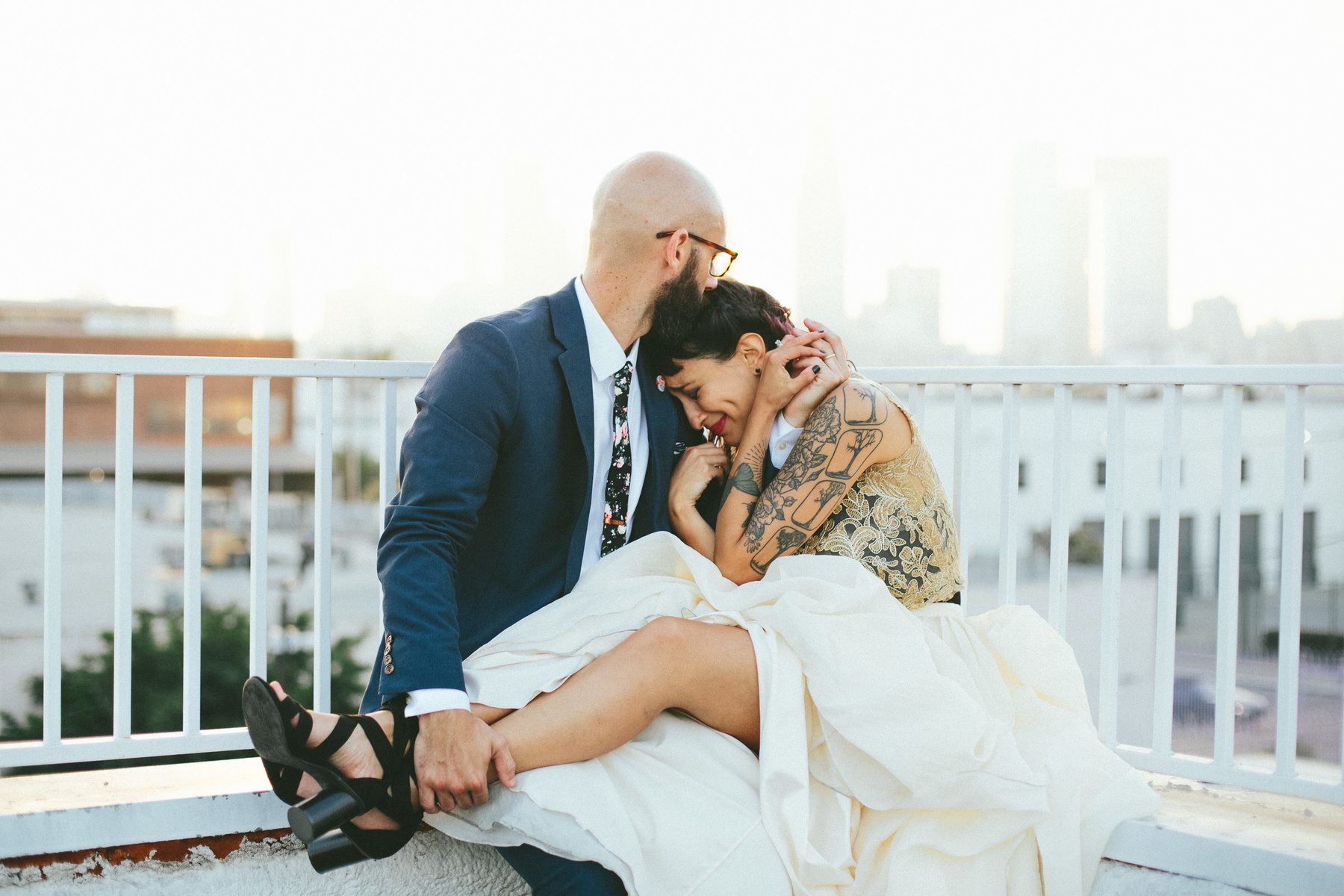 a man comforts a bride while she cries, a city skyline is in the distance