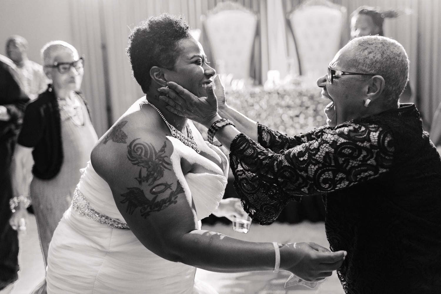 a bride and an older woman reach out their arms to each other, smiling, to embrace