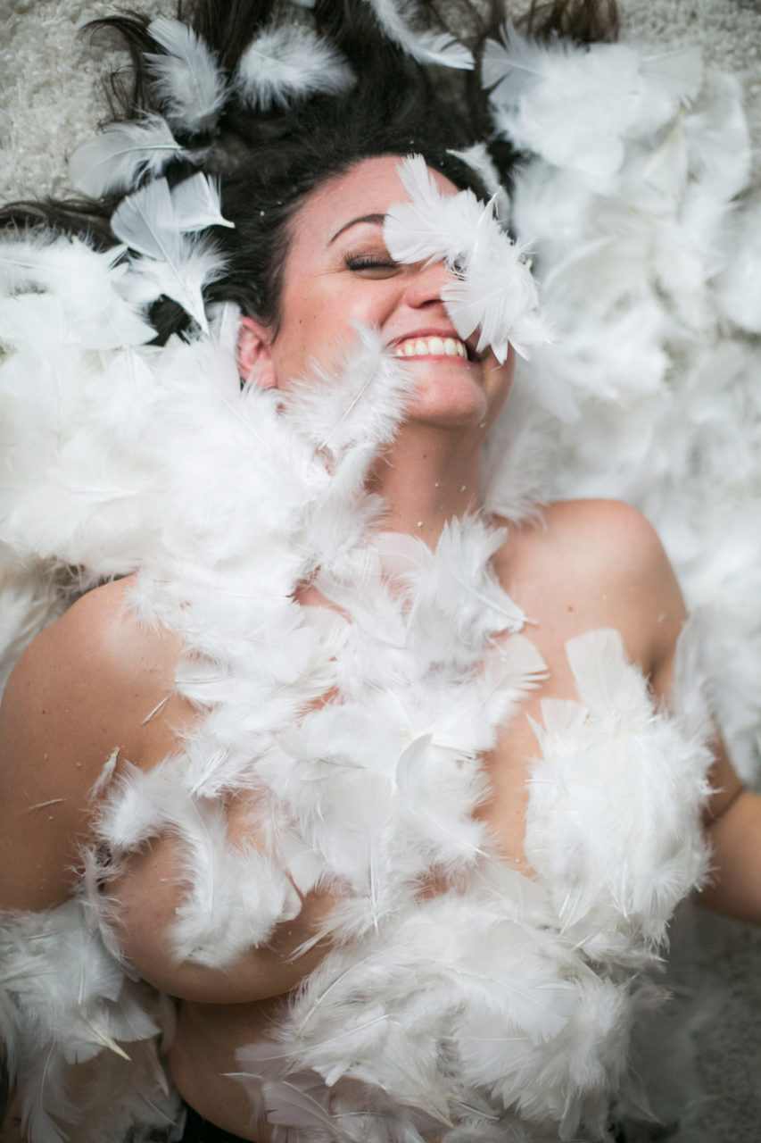 a woman lying nude & covered in feathers, alive