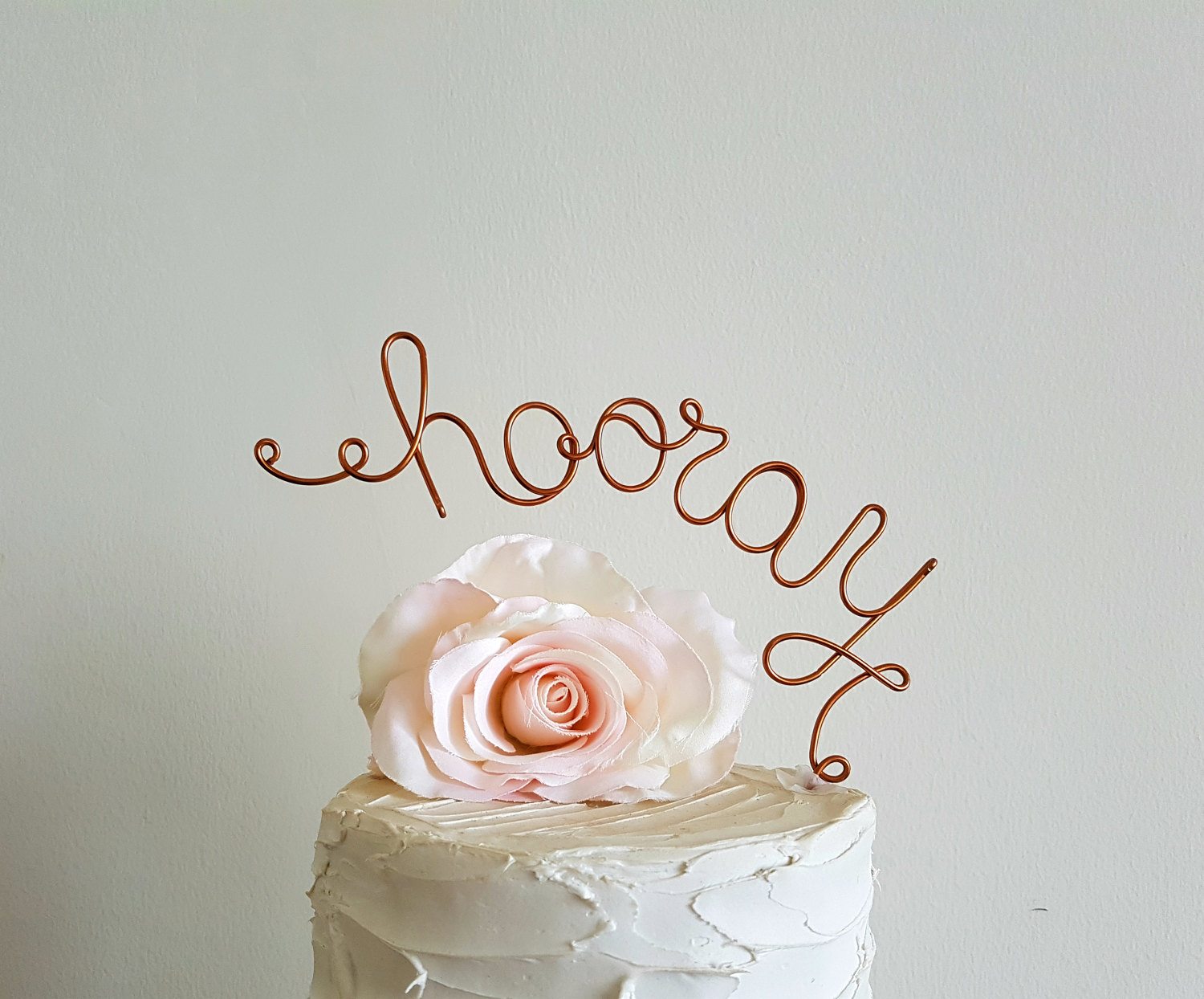 copper wire that says "hooray" cake topper and a flower