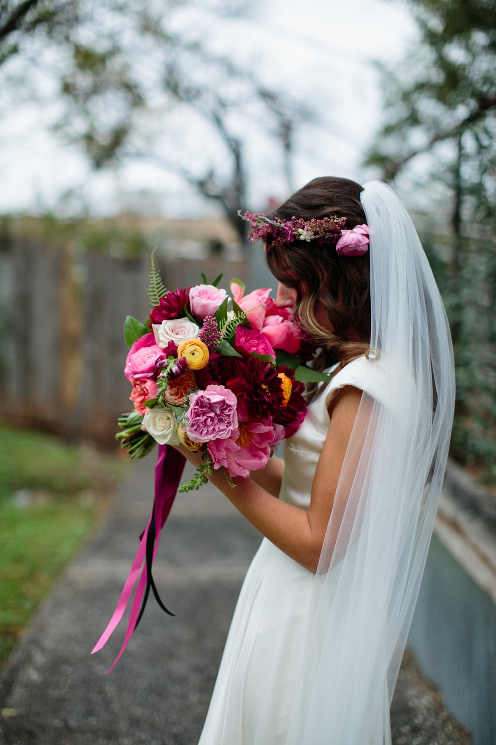 a woman smells her lush pink, yellow, and dark red hand-tied flower bouquet