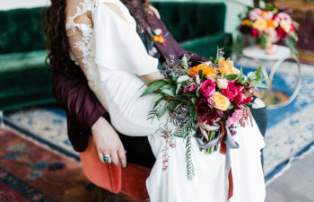 person in wedding dress holding colorful bouquet sits on partner's lap in an elegant indoor setting