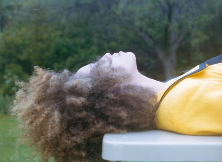 person in yellow laying down outside, with curly, kinky hair partially blocking face