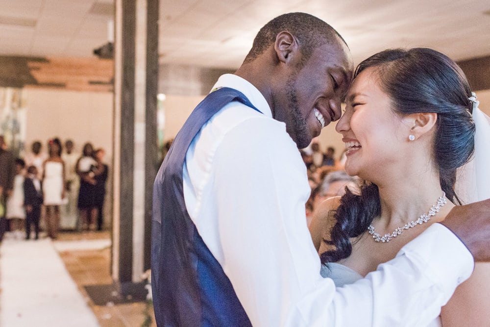 a couple smiles, resting foreheads together as they dance at a reception