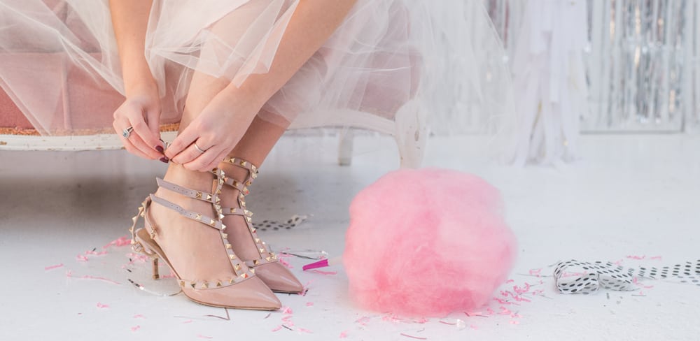 Close of a woman in a tulle skirt putting on her party shoes next to pink cotton candy