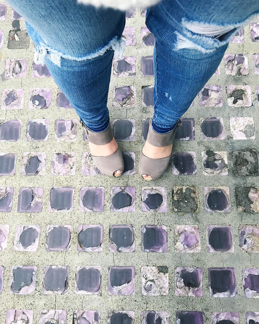 a woman's legs in jeans with ripped knees and grey-taupe open-toed clogs