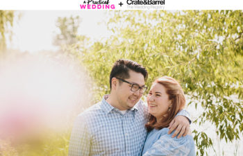 A couple embrace in the sun, smiling, near a tree