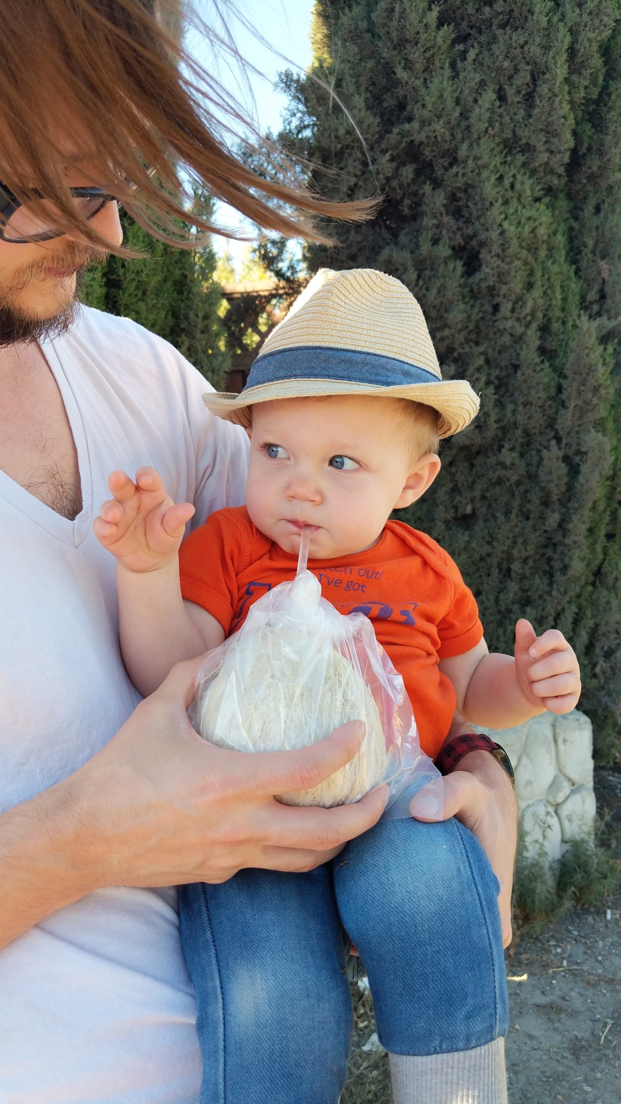 A man holds a baby as the baby drinks from a straw