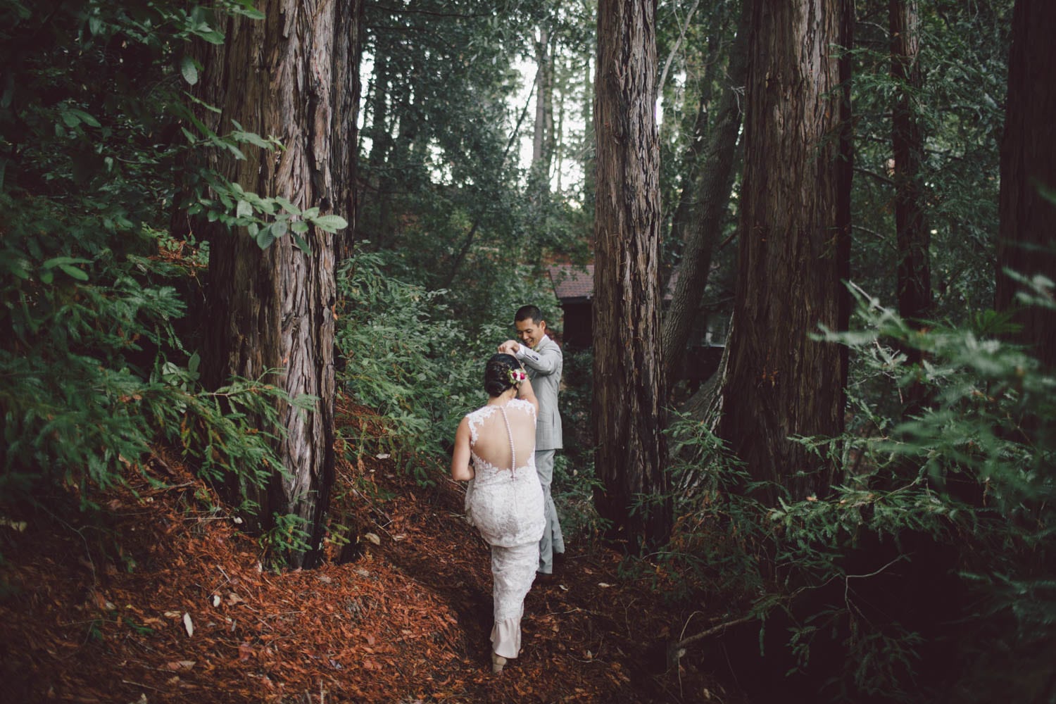 a bride in a backless dress and groom in a grey suit happily venture into the Redwood forest