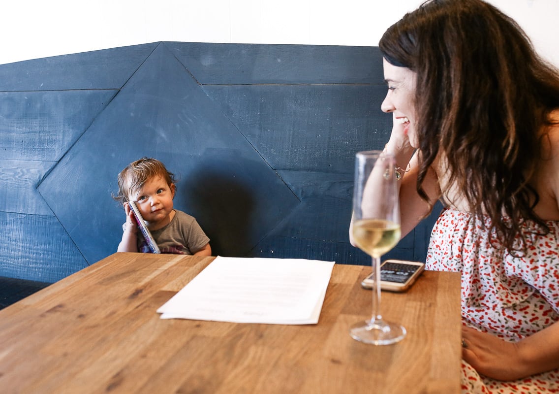 A woman smiles at a young child talking on a phone.