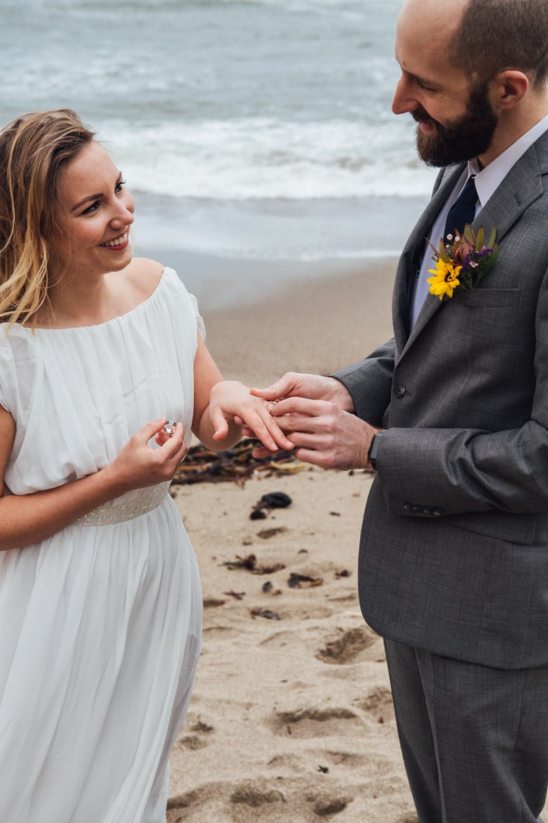 A man and woman exchange rings on a beach