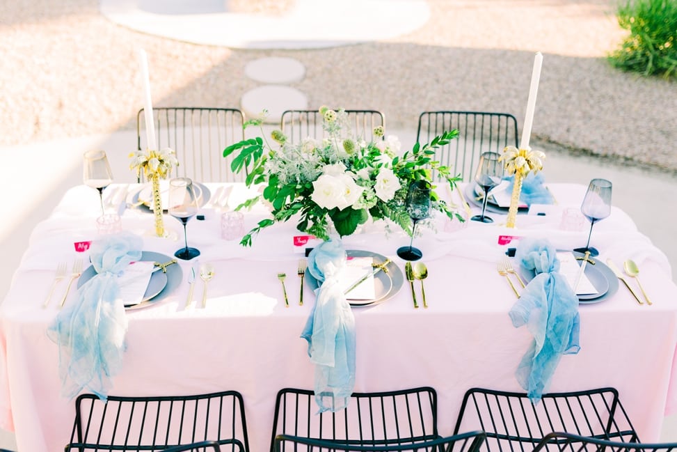 game of thrones inspired tablescape with pink tablecloth and blue silk napkins with palm tree candleholders and sword letter openers