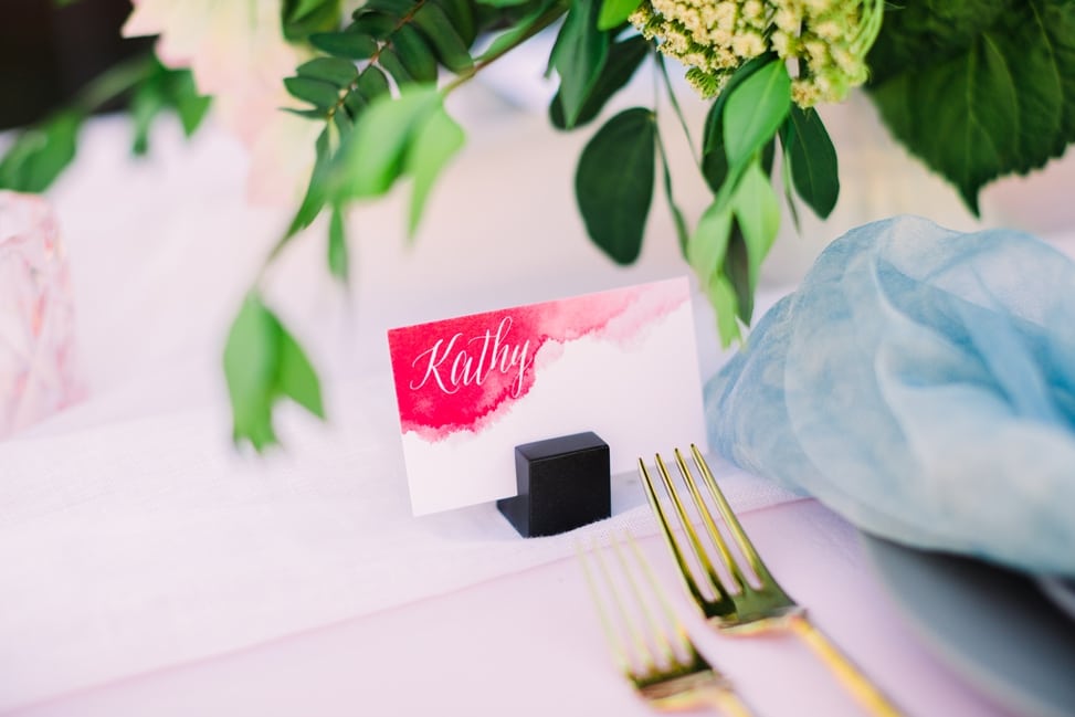 a close shot of a watercolor-style oxblood place card that reads "Kathy" in white calligraphy
