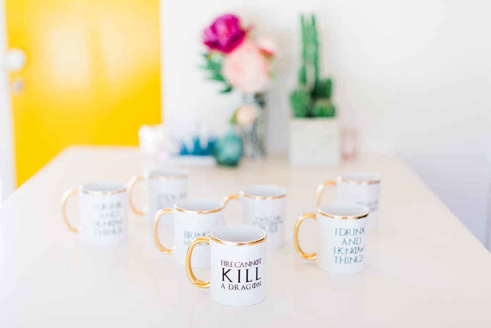 gold rimmed coffee mugs with game of thrones quotes on them sitting on top of a white counter top with a yellow door in the background