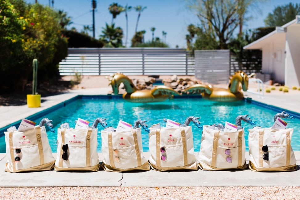 personalized embroidered tote bags with sunglasses, weekend itineraries, and inflatable dragon pool cupholders in front of a pool with gold dragon floaties