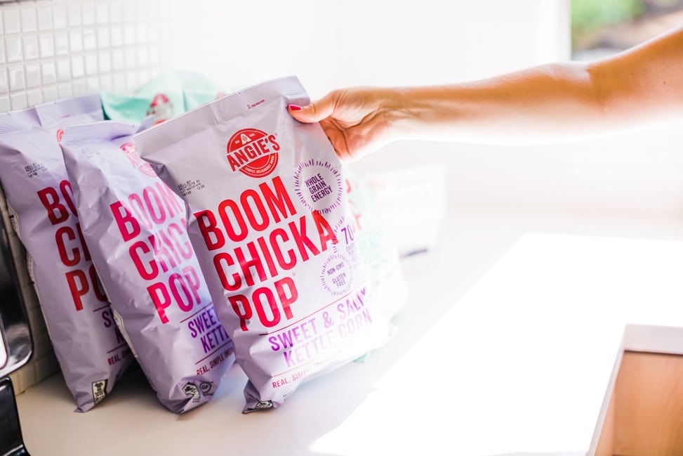 a woman reaches for a purple bag of Boom Chicka Pop in a brightly lit kitchen