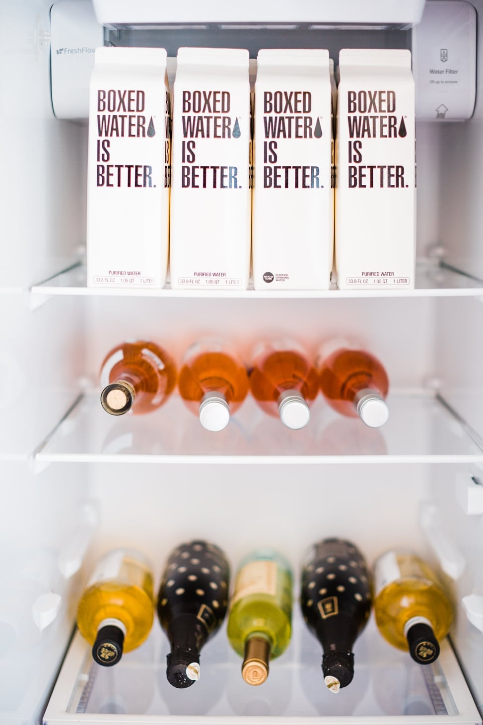 The inside of a fridge stocked with boxed water, rose, white wine, and sparkling wine