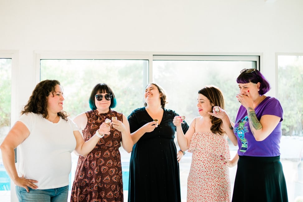 five women making faces after taking shots from mini goblets, in front of a window