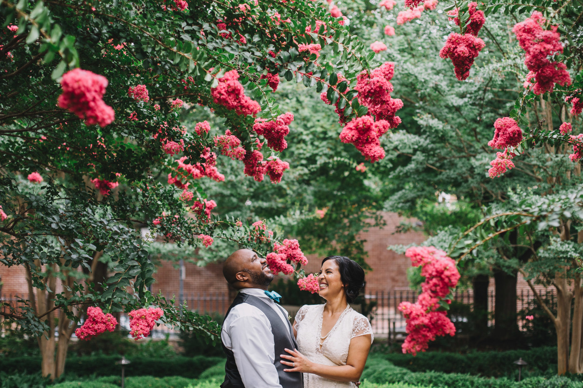 A couple laughs in a vibrant green and pink garden. Rachel Couch for Pop! Wed Co.