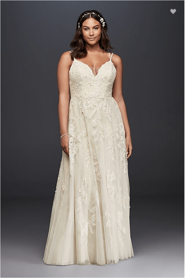 A woman wears an off-white wedding dress with double spaghetti straps and a sheer embroidered flower overlay with a peekaboo v-neck