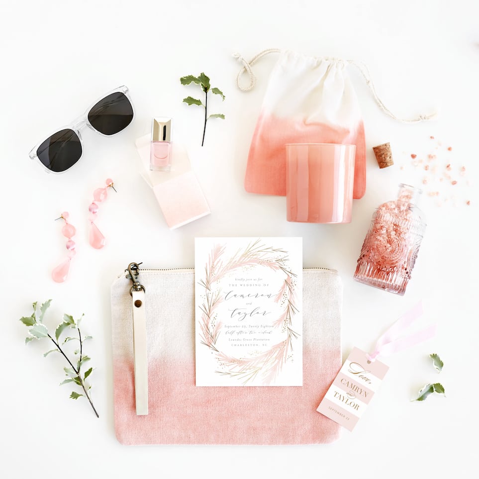 a collection of light pink, peach, and white items, including a dip-dyed clutch, a candle, a dip-dyed cloth bag, pink nail polish in an ombre box, pink earrings, an invitation and a gift tag from minted