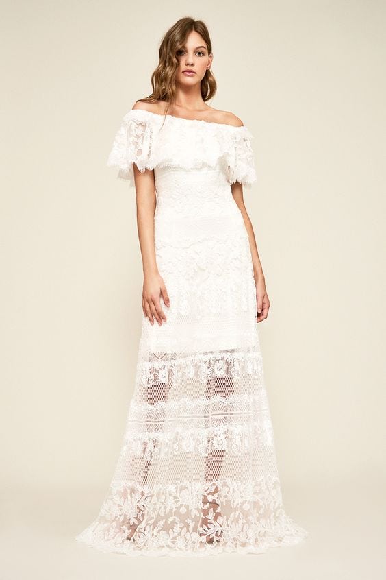 A woman wears a white lace dress with off-the-shoulder ruffle bodice