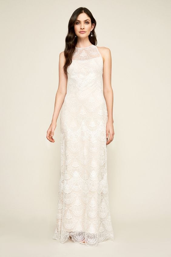 A woman wears a strapless white column dress with a high-neck sleeveless 20s-inspired lace overlay