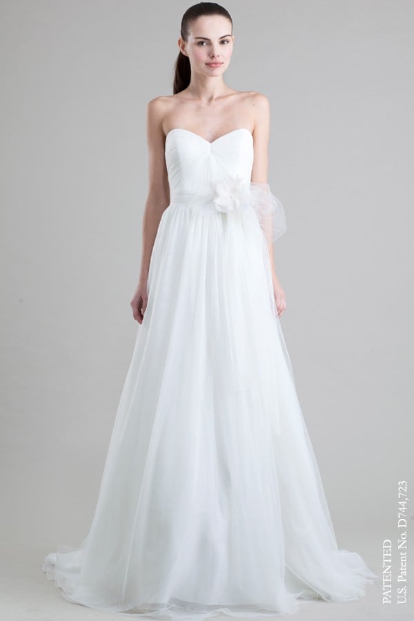 A woman wears a strapless white dress with a straight but full tulle skirt and tulle bow on the front side waist