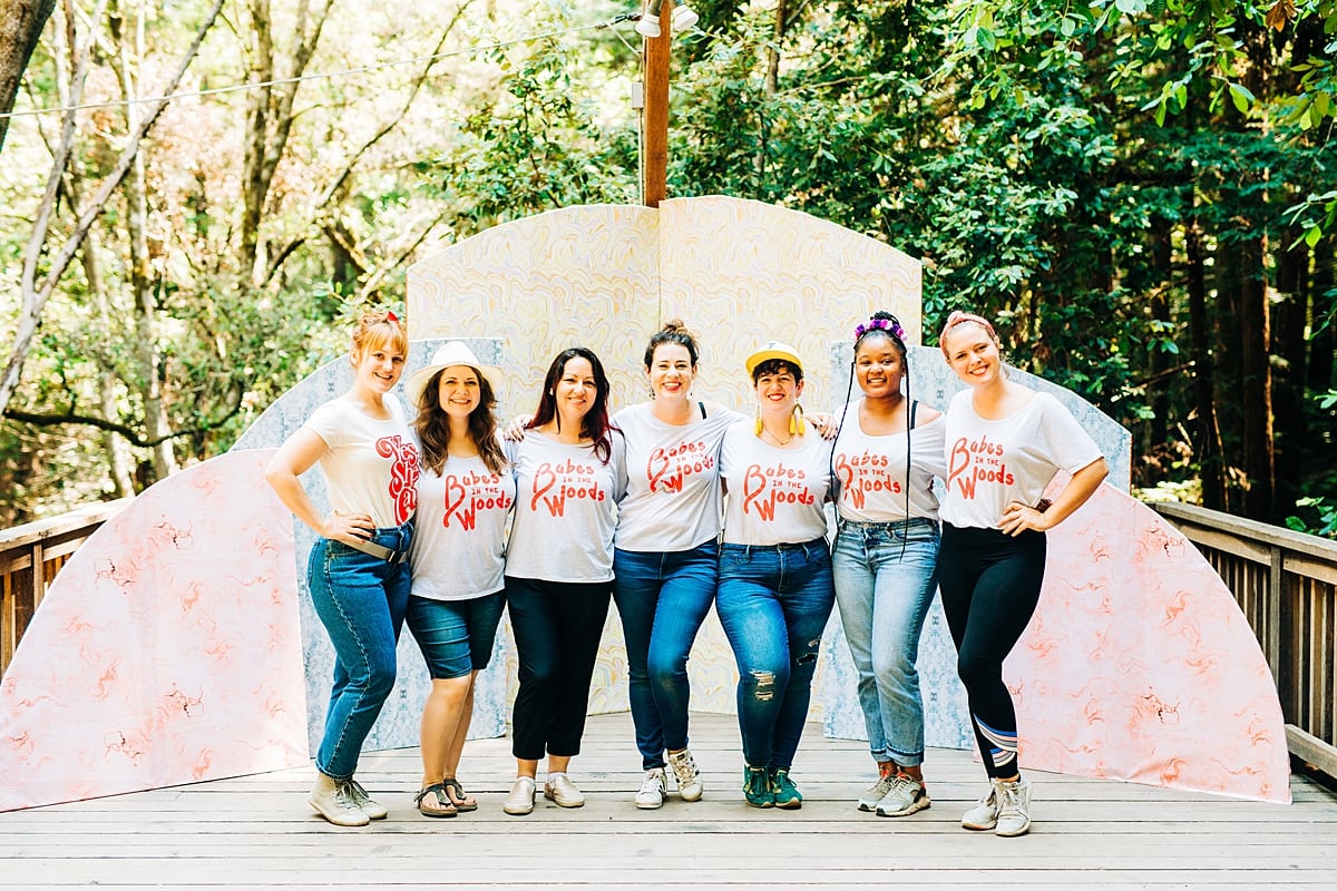 Seven women, camp staff, wearing babes in the woods teeshirts, standing in front of the sun rise paper installation at the compact summer camp in la Honda, CA