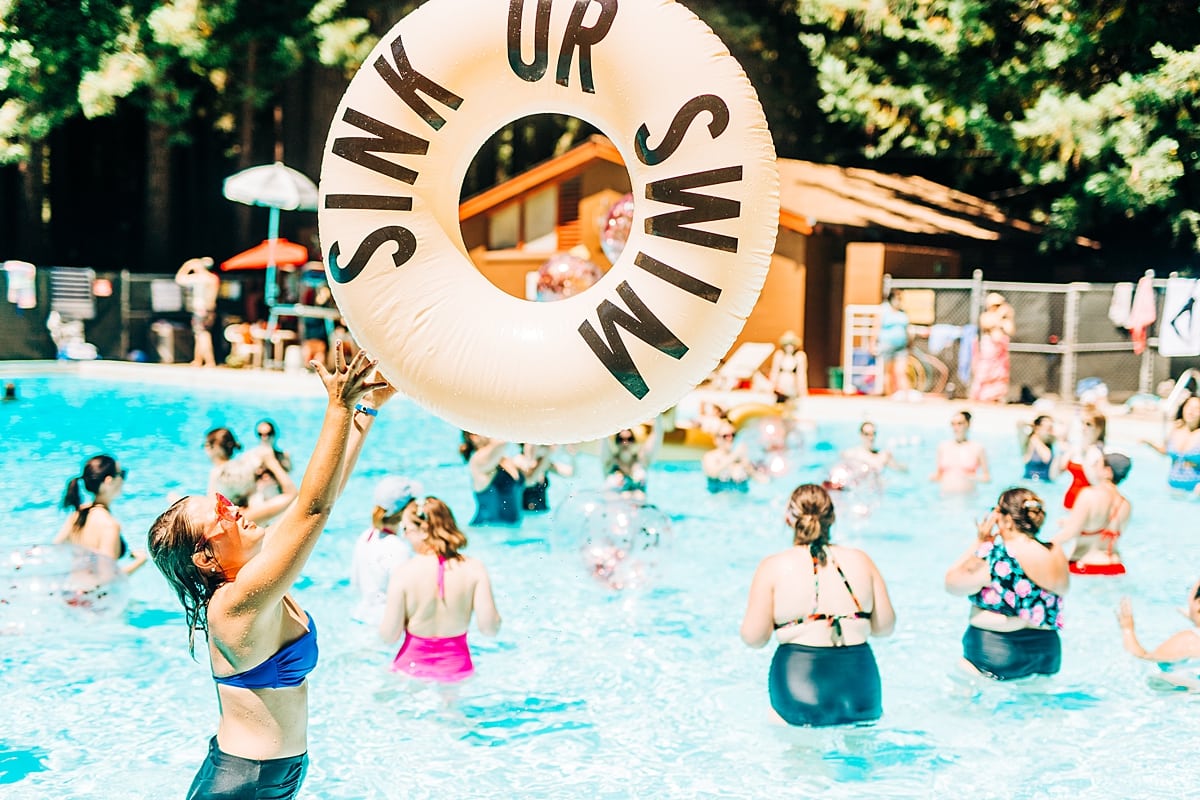 A woman tossing a large round floaty that reads Sink or Swim at the compact summer camp in la Honda, CA