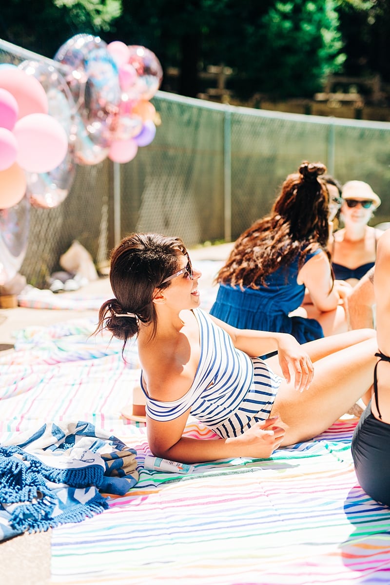 A woman in a striped swim suit smiling and lounging on a colorful towel at the compact summer camp in la Honda, CA