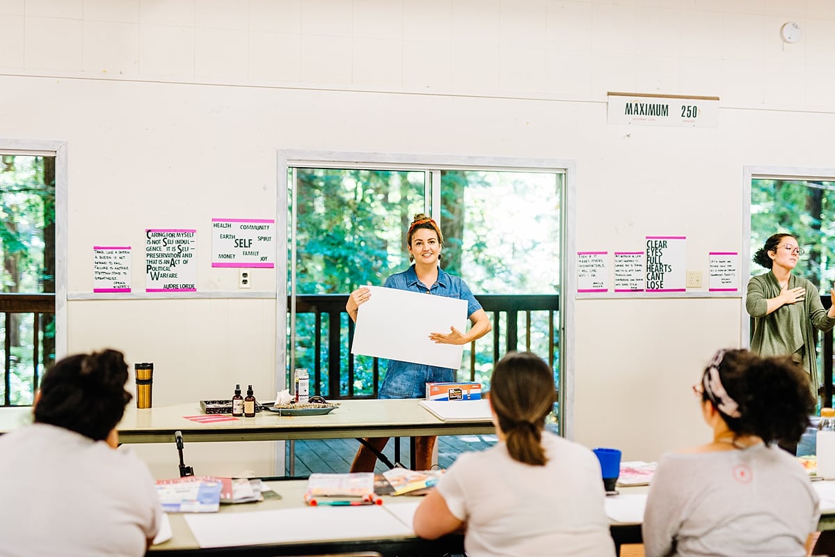 Eve Sturges presenting how to vision board in a brightly lit room, as a sign language interpreter signs nearby at the compact summer camp in la Honda, CA