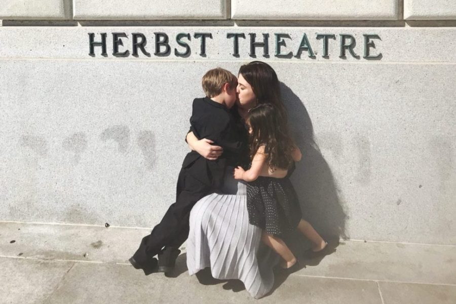 A woman embracing and kissing her two small children in front of the Herbst Theatre