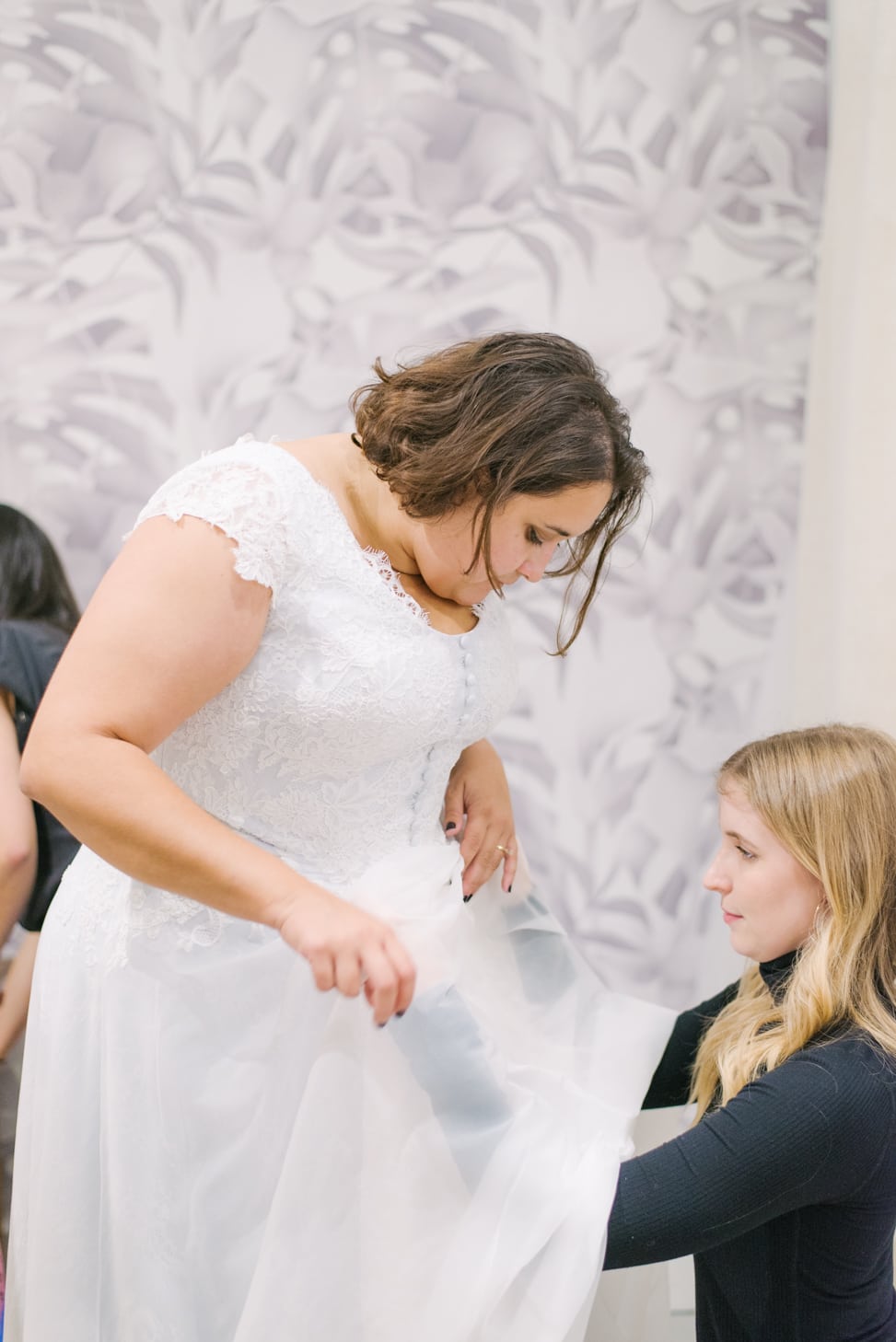 Plus size woman with short brunette hair getting her wedding dressed measure by a woman with long blonde hair in a black long sleeve shirt