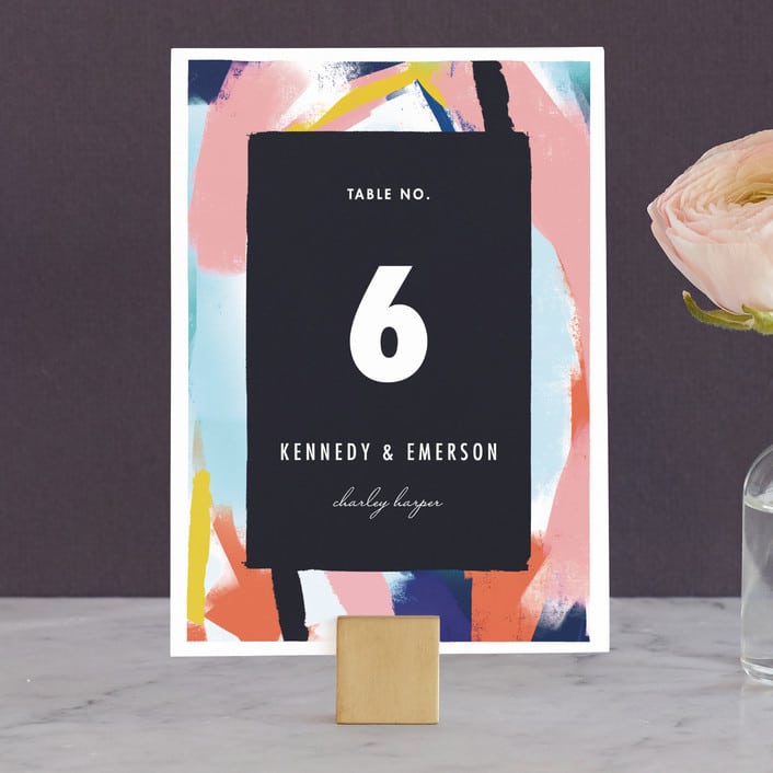 an abstract painting inspired table number from minted styled on a gold place card holder with a pink flower out of frame
